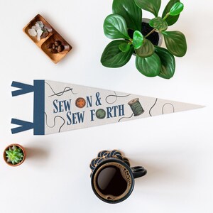a sewing kit with the text "Sew on & Sew Forth" printed on it, along with illustrations of sewing materials. The sewing kit is placed on a white surface, accompanied by a potted plant, a cup of coffee, and a small bowl of decorative items.