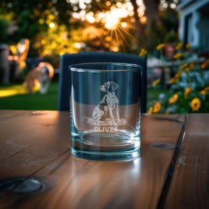 May include: A clear glass tumbler featuring an etched illustration of a seated dog and the name OLIVER engraved below the animal. The glass has a thick base and straight sides, designed for serving beverages in a standard drinking vessel format.
