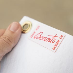 A hand holding a white tag with a red logo and text on it.