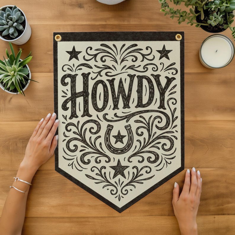 a banner with the word "HOWDY" written on it, surrounded by decorative elements such as stars and a horseshoe. The banner is placed on a wooden surface, with a pair of hands resting on it. There are also some potted plants and a candle in the background.