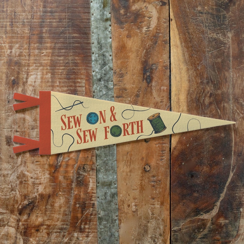 A beige pennant banner with the text "Sewon & Sewforth" printed on it, placed on a wooden surface.
