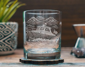 May include: A clear glass tumbler with an etched design of a boat sailing on water, with clouds in the background. The glass sits on a wooden coaster. The tumbler is approximately 4 inches tall.