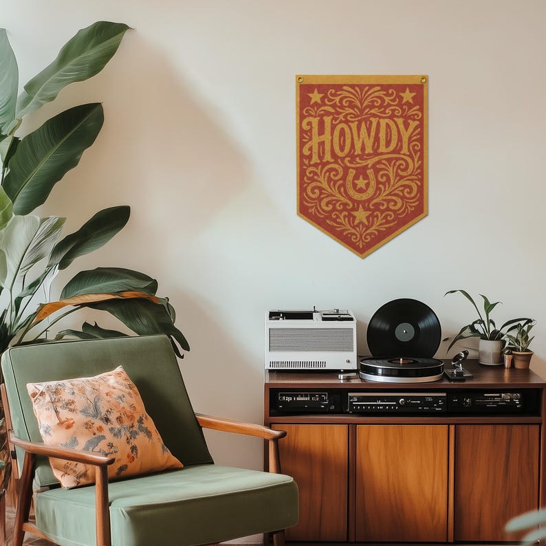 a cozy living room with a green armchair, a wooden cabinet with a turntable and speakers, and a large potted plant. A decorative banner with the word "HOWDY" in an ornate font hangs on the wall above the cabinet.