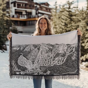 Può includere: Una donna tiene in mano una coperta in tessuto bianco e nero con una mappa dettagliata di una stazione sciistica. La mappa mostra le piste da sci e gli impianti di risalita di Red Mountain.
