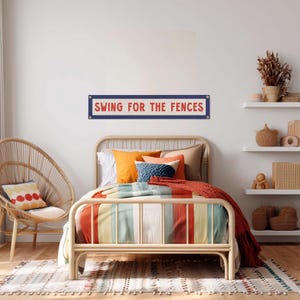 a bedroom with a bed, a wicker chair, and shelves with decorative items. A sign on the wall says "Swing for the Fences".