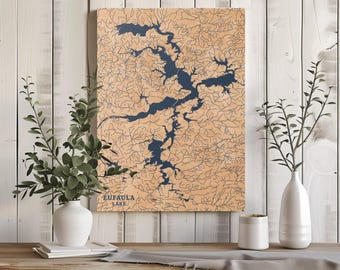 May include: A wooden map of Eufaula Lake with blue water and brown land. The map is framed and hanging on a white wood wall.