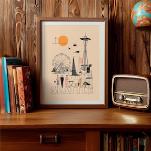 May include: A framed art print featuring a vintage-style illustration of Seattle landmarks, including the Space Needle, a Ferris wheel, and the city's name in bold letters. The artwork has a retro aesthetic with a warm color palette and is displayed on a wooden surface.