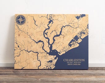 May include: A wooden map of Charleston, South Carolina, with blue water features and a compass rose in the top left corner. The text "CHARLESTON, EAST COAST - UNITED STATES, SOUTH CAROLINA" is printed in white at the bottom right corner.