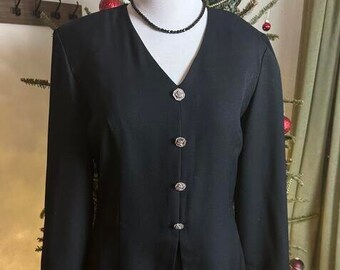 May include: A black skirt suit with a v-neckline and silver buttons. The suit is on a mannequin and is displayed in front of a Christmas tree.