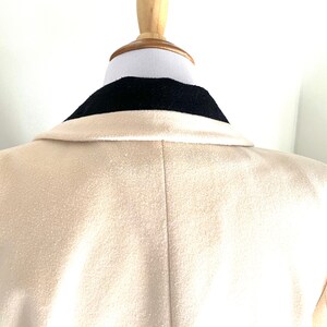 K&ouml;nnte beinhalten: Ein cremefarbener Blazer mit einem schwarzen Samtkragen. Der Blazer ist aus einem weichen, strukturierten Stoff gefertigt.