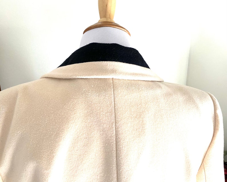 K&ouml;nnte beinhalten: Ein cremefarbener Blazer mit einem schwarzen Samtkragen. Der Blazer ist aus einem weichen, strukturierten Stoff gefertigt.