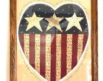 May include: A framed heart-shaped fabric applique featuring a blue field with stars and red and white stripes. The text "I pledge allegiance to the flag of the United States of America and to the republic for which stands, one nation under God, indivisible, with liberty and justice for all" is written around the heart, signed "Shirley Wolf 2002".
