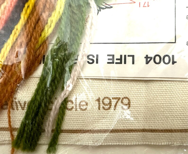 May include: A close-up of a cross-stitch kit with a beige canvas, brown and green embroidery floss, and the text "1004 LIFE IS" and "Circle 1979".
