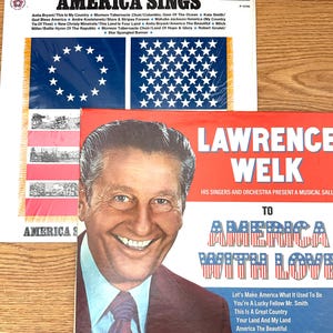 Op de afbeelding: Twee vinyl platenhoezen getiteld America Sings en Lawrence Welk To America With Love. De hoes van America Sings toont een blauwe vlag met witte sterren en een tracklist. De hoes van Lawrence Welk bevat een portret van de artiest.