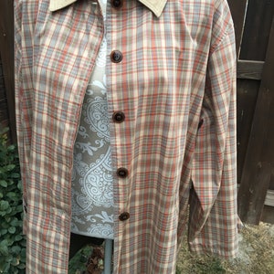 May include: A long, beige and orange plaid jacket with a corduroy collar. The jacket has a button-up front and long sleeves.