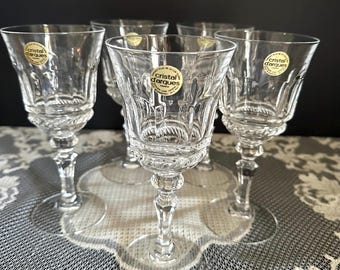 May include: A set of five clear crystal stemmed glasses featuring a faceted bowl design and a textured stem. Each glass displays a circular gold and white sticker with the text Cristal d'Arques France, indicating the manufacturer and origin.