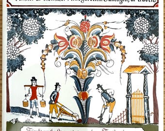 May include: A square ceramic tile featuring a hand-painted scene of three figures in a garden with a large central floral motif. The top text reads Vänner är blommor i trädgarden... Familjen, är träden and the bottom text reads Friends are the flowers in our gardens... Family, the trees.