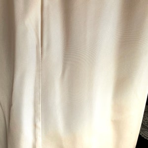 K&ouml;nnte beinhalten: Nahaufnahme eines wei&szlig;en Stoffes mit einer subtilen Textur. Der Stoff hat einen leichten Glanz und wirkt glatt und weich.