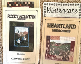 Könnte beinhalten: Vier Quilting-Musterbücher mit braunen Umschlägen und weißem Text. Die Titel lauten "Heartland Memories", "Rocky Mountain Memories", "Winterscape" und "Heartland Memories". Das Buch rechts zeigt ein Bild eines Bauernhofs mit einem roten Scheunentor und grünen Feldern. Das Buch darunter zeigt ein Bild einer Bergkette mit blauem Himmel und weißen Wolken. Das Buch links zeigt ein Bild eines karierten Musters. Das Buch in der Mitte zeigt ein Bild einer Blume.