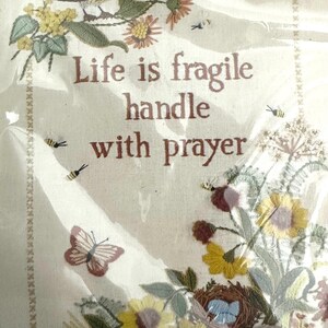 May include: Embroidered wall art with a bird, flowers, and butterflies. The text reads "Life is fragile handle with prayer".