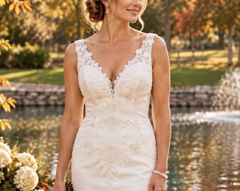 May include: A sleeveless white wedding dress featuring a deep V-neckline, intricate floral lace appliques on the bodice, and a row of small buttons running down the centre. The gown has a fitted silhouette with detailed embroidery extending to the waist.