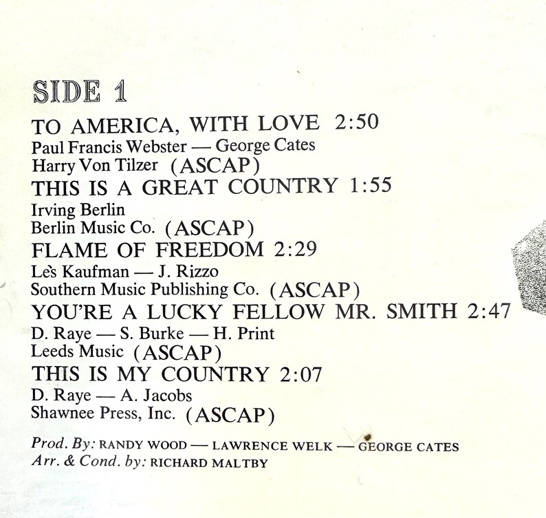 Op de afbeelding: Een tracklist op wit papier met de titel SIDE 1 en zwarte tekst. De nummers zijn onder andere TO AMERICA, WITH LOVE, THIS IS A GREAT COUNTRY, FLAME OF FREEDOM, YOU'RE A LUCKY FELLOW MR. SMITH en THIS IS MY COUNTRY met bijbehorende credits.