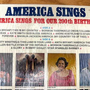 Op de afbeelding: Een vinylplatenhoes met de titel America Sings For Our 200th Birthday. De hoes bevat blauwe en rode tekst, een tracklist voor kant A en kant B, en vier rechthoekige foto's van artiesten, waaronder Anita Bryant en Kate Smith.