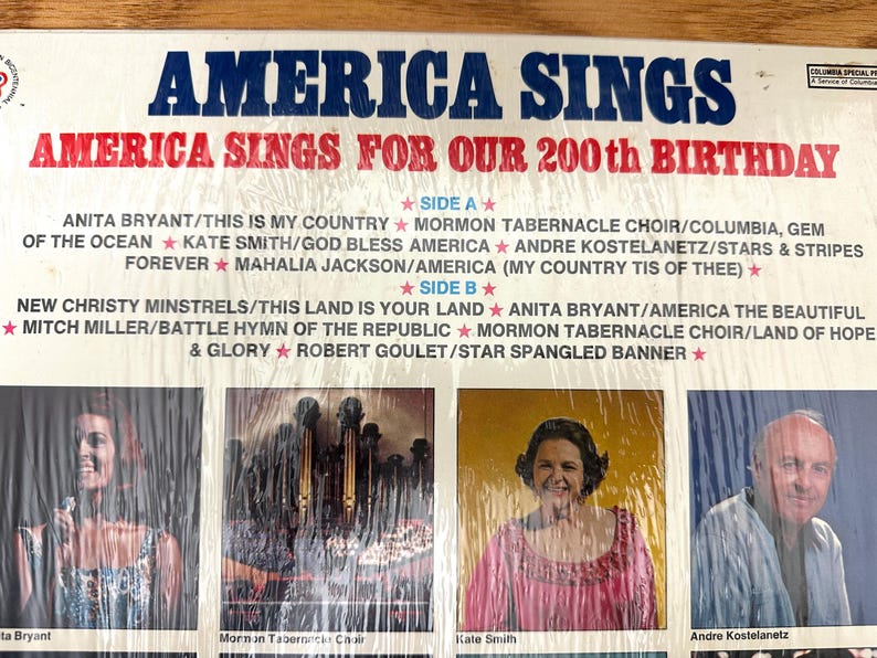 Op de afbeelding: Een vinylplatenhoes met de titel America Sings For Our 200th Birthday. De hoes bevat blauwe en rode tekst, een tracklist voor kant A en kant B, en vier rechthoekige foto's van artiesten, waaronder Anita Bryant en Kate Smith.