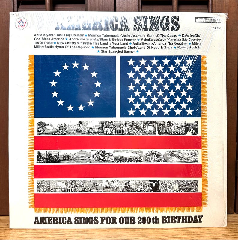 Op de afbeelding: Een vinyl hoes getiteld America Sings met een blauw veld met witte sterren, rode en witte strepen en zwart-witte historische illustraties. De tekst bevat songtitels en de tekst America Sings For Our 200th Birthday.