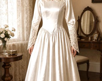 May include: A floor-length cream-coloured satin dress featuring long sleeves with intricate lace cuffs, a matching lace collar, a fitted bodice with a V-shaped waistline, and a full, pleated skirt that flows down to the floor in a smooth, lustrous finish.