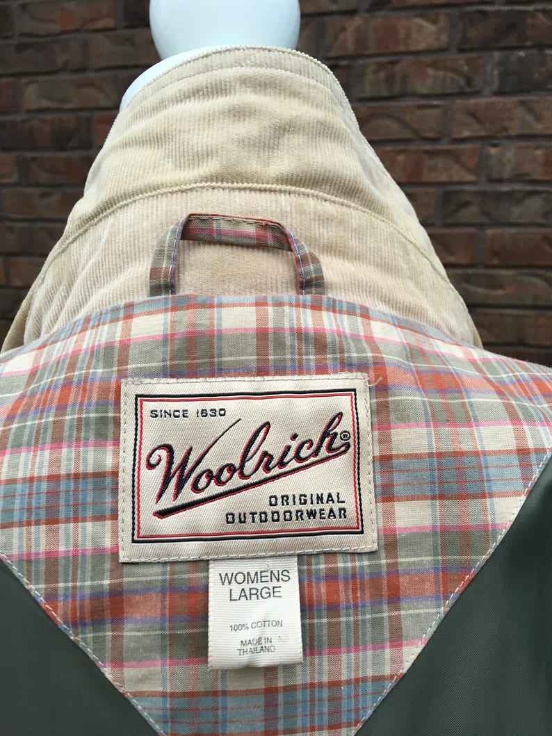 May include: A green jacket with a plaid lining and a Woolrich label. The label says "Since 1830 Woolrich Original Outdoorwear" and "Womens Large 100% Cotton Made in Thailand".