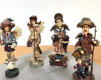 May include: Four decorative figurines featuring stylised characters: a golfer with a blue sweater, a baseball player with wings, a baker holding a tray with the text 'Life is short, eat dessert first', and a fisherman with a child holding a fishing rod.
