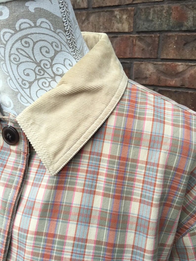 May include: A plaid shirt with a corduroy collar. The shirt is a light beige color with pink, blue, and orange plaid.