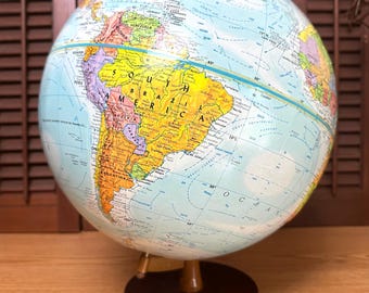 May include: A vintage globe with a detailed map of the world, mounted on a dark wooden base. The globe features a light blue ocean and colorful continents, with visible country names and borders. The globe is approximately 12 inches in height.