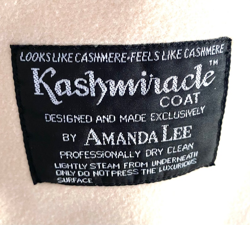 K&ouml;nnte beinhalten: Ein schwarzes und wei&szlig;es Etikett mit dem Text "LOOKS LIKE CASHMERE FEELS LIKE CASHMERE" und "Kashmiracle COAT" in einer stilisierten Schriftart. Das Etikett enth&auml;lt auch den Text "DESIGNED AND MADE EXCLUSIVELY BY AMANDA LEE" und "PROFESSIONALLY DRY CLEAN LIGHTLY STEAM FROM UNDERNEATH ONLY DO NOT PRESS THE LUXURIOUS SURFACE".