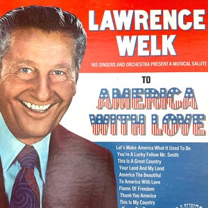 Op de afbeelding: Een vintage vinyl platenhoes met een portret van Lawrence Welk aan de linkerkant. De tekst luidt LAWRENCE WELK HIS SINGERS AND ORCHESTRA PRESENT A MUSICAL SALUTE TO AMERICA WITH LOVE, gevolgd door een tracklist inclusief America The Beautiful.