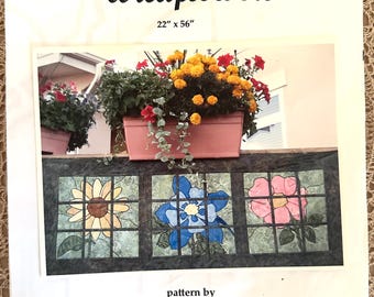 Könnte beinhalten: Ein Bastelmuster für eine Steppdecke mit drei Bleiglas-artigen Paneelen mit Bildern einer Sonnenblume, einer blauen Blume und einer rosa Blume. Das Muster trägt den Titel "Favorite Colorado Wildflowers" und ist 56 cm x 142 cm groß. Das Muster stammt von Toni & Juanita, Littleton, Colorado.