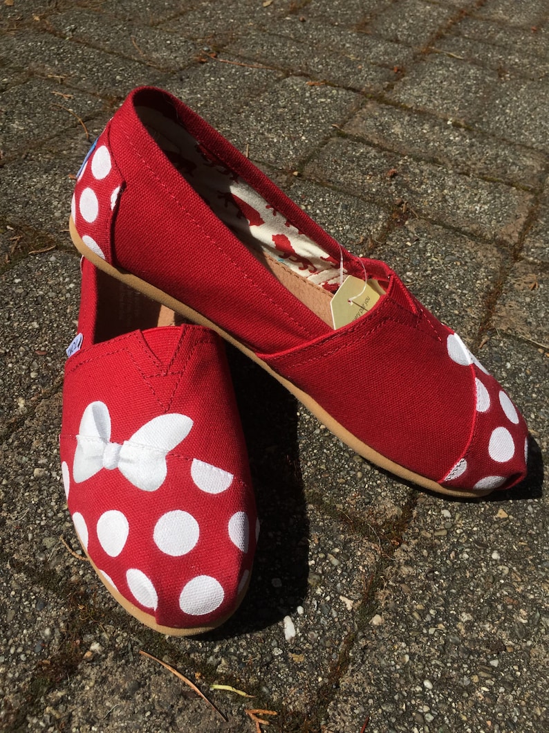 May include: A pair of red canvas shoes with white polka dots and a white bow on the toe.