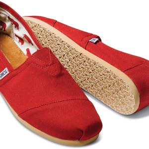 May include: A pair of red canvas slip-on shoes with a brown sole and the word "TOMS" on the side.