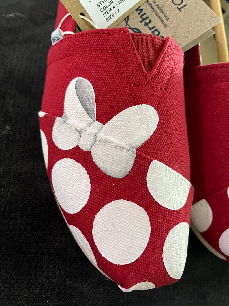 May include: Red canvas shoes with white polka dots and a white bow painted on the toe. The shoes are size 7.
