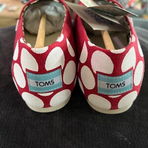 May include: A pair of red and white polka dot canvas shoes with the word "TOMS" on the side of each shoe.