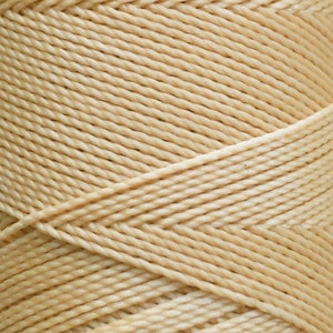 May include: A spool of beige waxed cotton cord. The cord is wound tightly and has a smooth, even texture.
