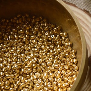 May include: A wooden bowl filled with gold-coloured beads. The bowl is sitting on a wooden base. A wooden mallet is lying on a brown fabric surface.