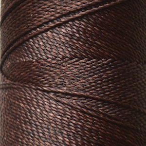 May include: A spool of brown waxed linen thread.