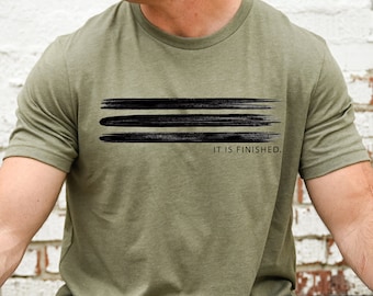 May include: A green t-shirt with a black brushstroke design and the text "IT IS FINISHED."