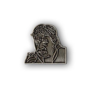 May include: Silver-toned metal pin featuring a line drawing of a man with a serious expression. The man is wearing a jacket and has short, wavy hair.
