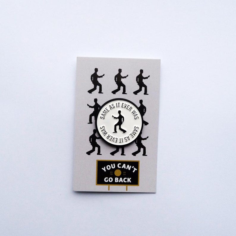 May include: White enamel pin with a black silhouette of a person dancing and the text "Same as it ever was" repeated around the edge. The pin is on a gray background with black silhouettes of people dancing. Below the pin is a black and white sign that says "You can't go back."