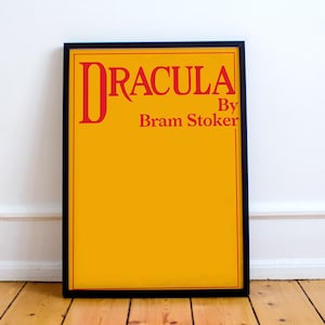 May include: A framed poster with a yellow background and black frame. The poster features the title "Dracula" in red text, followed by "By Bram Stoker" in smaller red text.