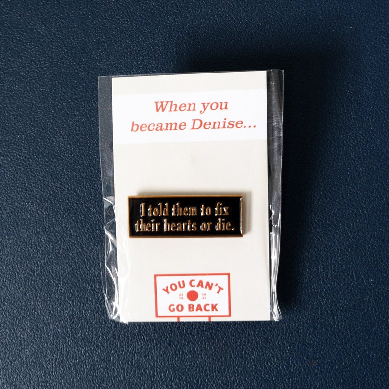 May include: Black enamel pin with gold lettering that reads "I told them to fix their hearts or die."  The pin is on a white card with the text "When you became Denise..." and "YOU CAN'T GO BACK" in red and black lettering.