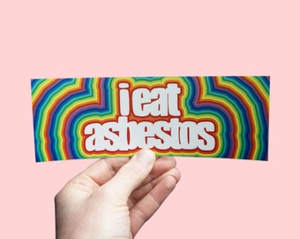 May include: A rainbow-colored sticker with the text "i eat asbestos" in white letters.